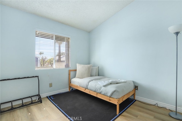 bedroom featuring a textured ceiling, wood-type flooring, and vaulted ceiling