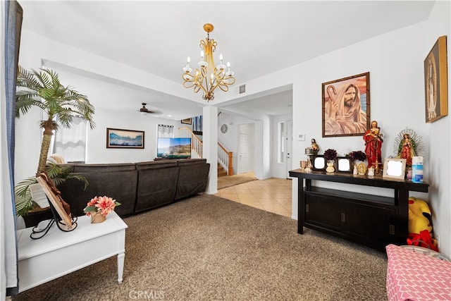 carpeted living room featuring ceiling fan with notable chandelier, stairway, tile patterned flooring, and visible vents