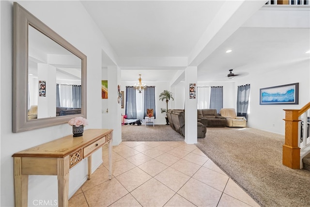 living room with ceiling fan with notable chandelier, light tile patterned flooring, light colored carpet, and stairs