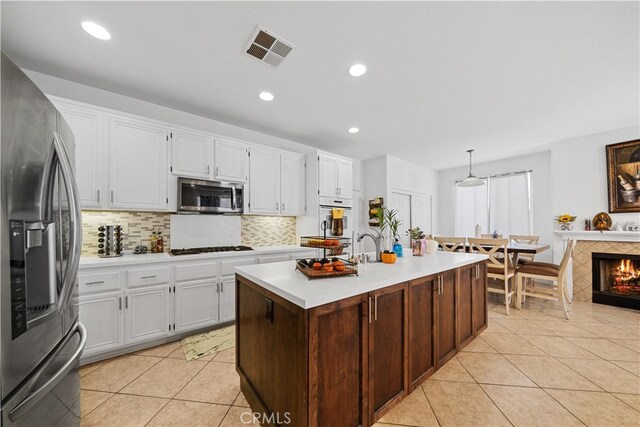 kitchen featuring light tile patterned floors, stainless steel appliances, light countertops, visible vents, and a tile fireplace