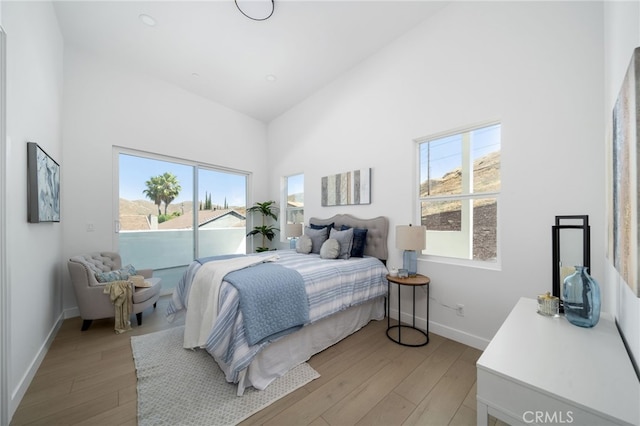 bedroom with a towering ceiling, light hardwood / wood-style flooring, and multiple windows