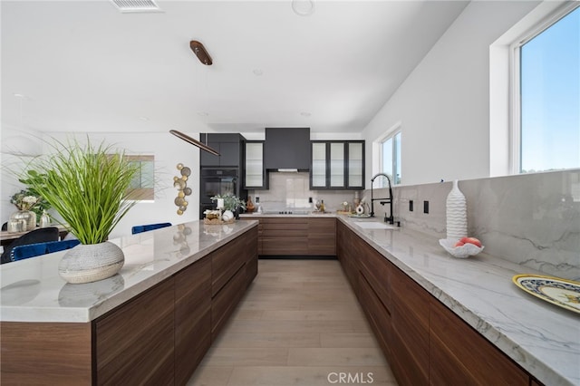 kitchen featuring black electric stovetop, tasteful backsplash, decorative light fixtures, light stone countertops, and sink