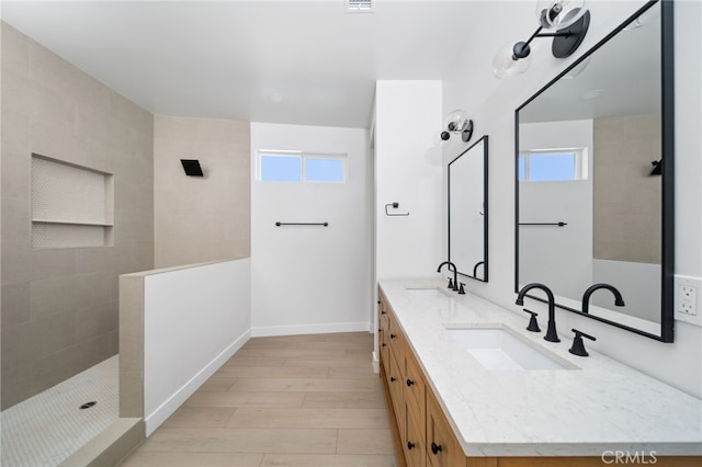 bathroom featuring vanity, wood-type flooring, a healthy amount of sunlight, and a tile shower