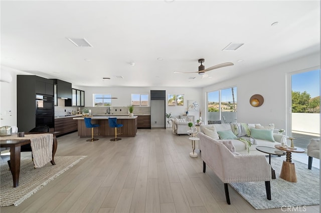 living room with ceiling fan, sink, and light wood-type flooring