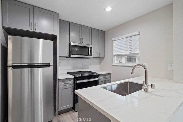 kitchen featuring gray cabinetry, light hardwood / wood-style floors, backsplash, stainless steel appliances, and sink