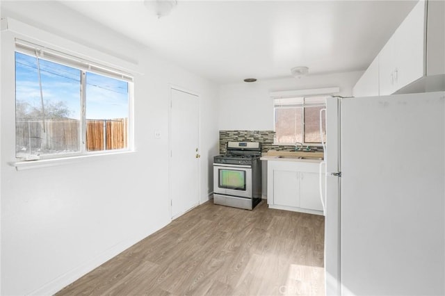 kitchen featuring gas stove, white cabinetry, white fridge, and a healthy amount of sunlight