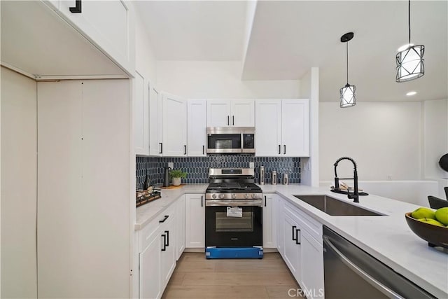 kitchen featuring appliances with stainless steel finishes, sink, decorative light fixtures, light hardwood / wood-style flooring, and white cabinetry