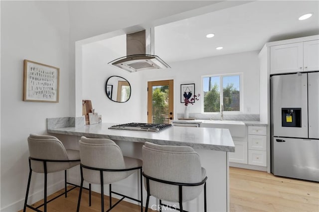 kitchen with island exhaust hood, light hardwood / wood-style floors, a kitchen bar, white cabinets, and appliances with stainless steel finishes