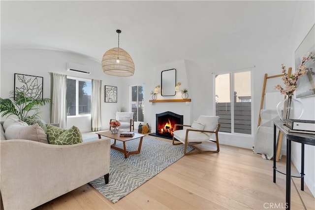 living room featuring a wall mounted air conditioner, light wood-type flooring, and vaulted ceiling