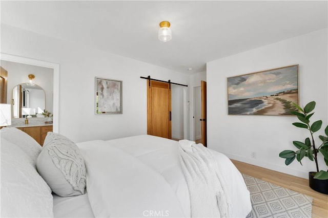 bedroom featuring a barn door, ensuite bathroom, and light wood-type flooring