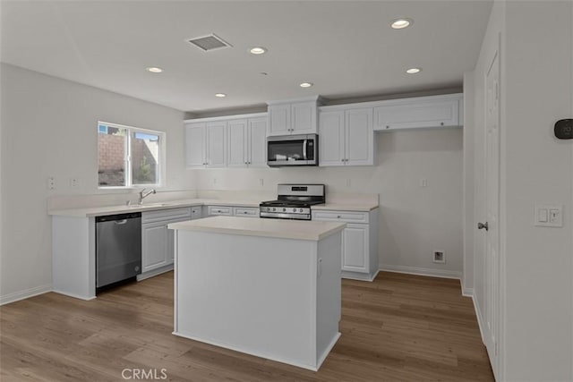 kitchen with white cabinets, a center island, stainless steel appliances, and light hardwood / wood-style floors