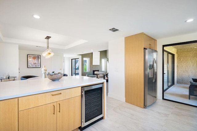 kitchen featuring light brown cabinets, hanging light fixtures, beverage cooler, stainless steel fridge with ice dispenser, and a raised ceiling