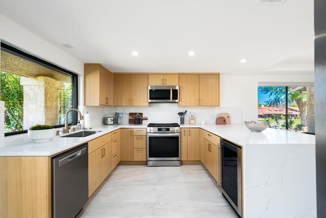 kitchen with appliances with stainless steel finishes, sink, light brown cabinetry, kitchen peninsula, and wine cooler