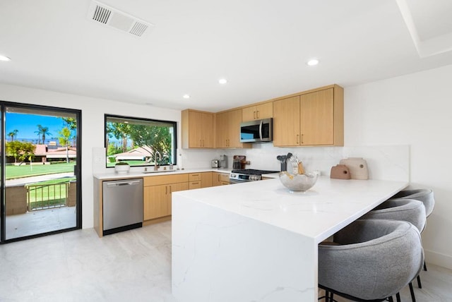 kitchen featuring sink, kitchen peninsula, stainless steel appliances, a breakfast bar area, and light brown cabinets