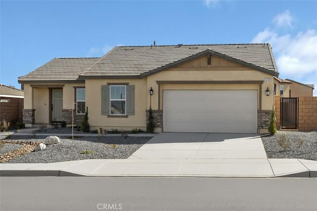 view of front of home featuring fence, a tiled roof, concrete driveway, stone siding, and an attached garage