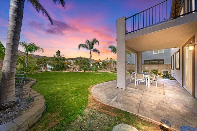 yard at dusk featuring a balcony and a patio