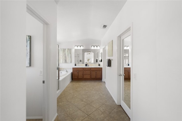 bathroom featuring a washtub, vanity, vaulted ceiling, and tile patterned flooring