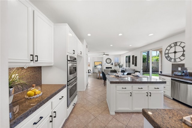 kitchen with appliances with stainless steel finishes, a kitchen island, ceiling fan, dark stone countertops, and white cabinetry