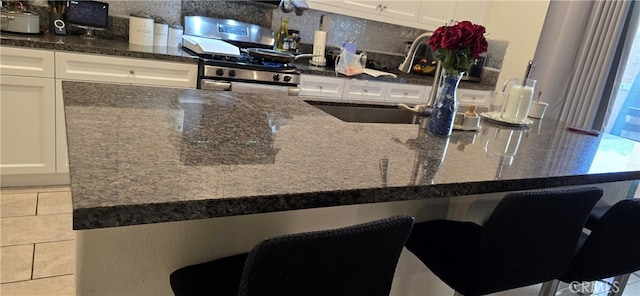 kitchen with a breakfast bar, gas range, sink, and white cabinets