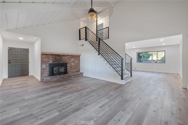 unfurnished living room featuring beam ceiling, a brick fireplace, light hardwood / wood-style flooring, high vaulted ceiling, and wooden ceiling