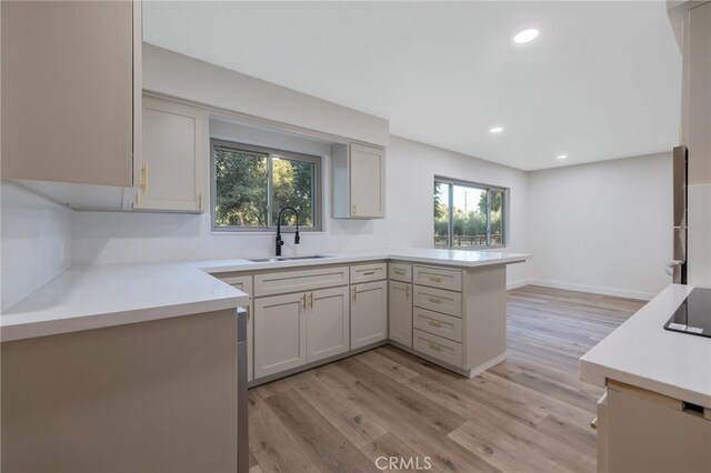 kitchen featuring a healthy amount of sunlight, kitchen peninsula, sink, and light hardwood / wood-style flooring