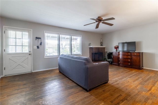 living room featuring a brick fireplace, dark wood-type flooring, and ceiling fan