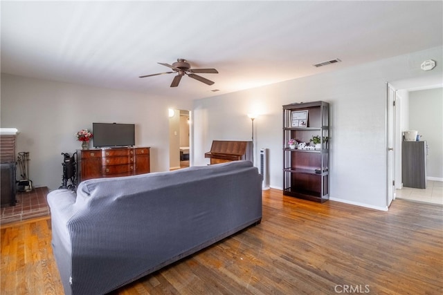 living room featuring ceiling fan, a wood stove, and wood-type flooring