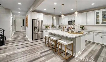 kitchen featuring pendant lighting, an island with sink, white cabinetry, appliances with stainless steel finishes, and a breakfast bar