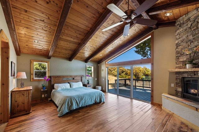 unfurnished bedroom featuring ceiling fan, vaulted ceiling with beams, wood ceiling, a stone fireplace, and hardwood / wood-style flooring