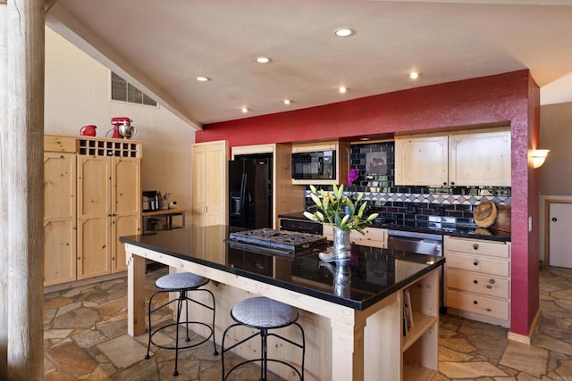 kitchen featuring light brown cabinetry, decorative backsplash, black appliances, and a kitchen bar