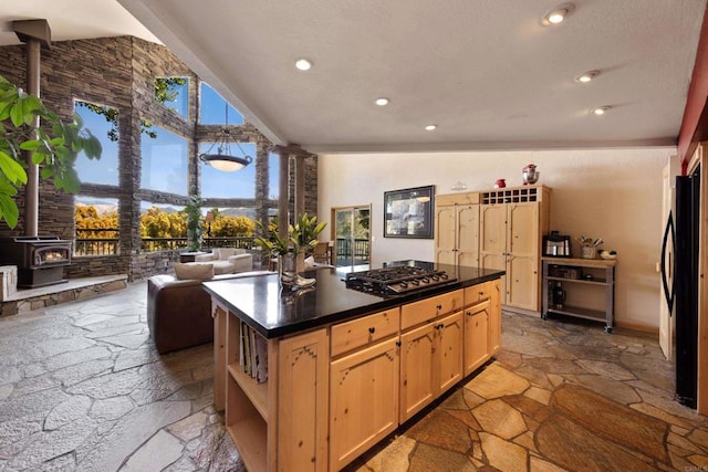 kitchen featuring a wood stove, black refrigerator, lofted ceiling, light brown cabinetry, and a center island