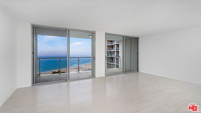 spare room featuring a beach view, a wall of windows, a water view, and a healthy amount of sunlight