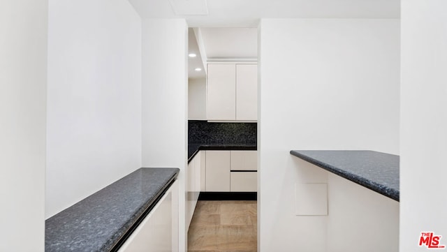 kitchen with light hardwood / wood-style floors, dark stone countertops, white cabinetry, and tasteful backsplash