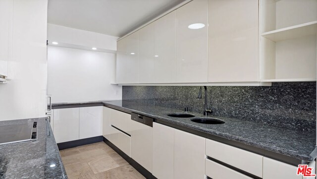 kitchen featuring sink, dishwashing machine, white cabinets, dark stone countertops, and decorative backsplash