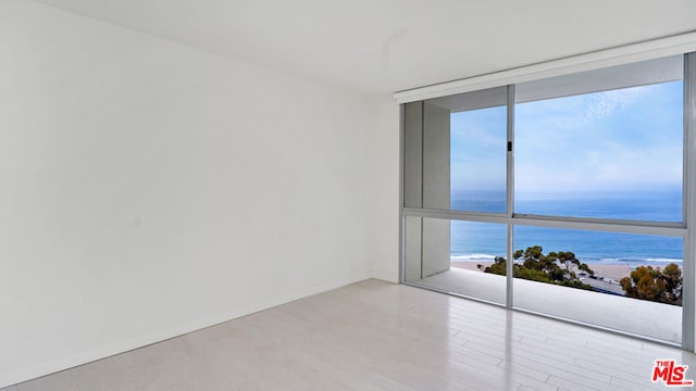 unfurnished room with light hardwood / wood-style floors, a wall of windows, a water view, and a beach view