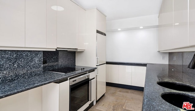 kitchen featuring oven, white cabinets, dark stone countertops, black electric stovetop, and white refrigerator