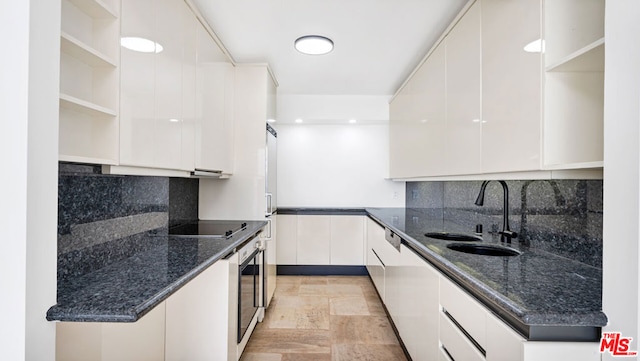 kitchen featuring oven, white cabinets, dark stone counters, black electric stovetop, and sink