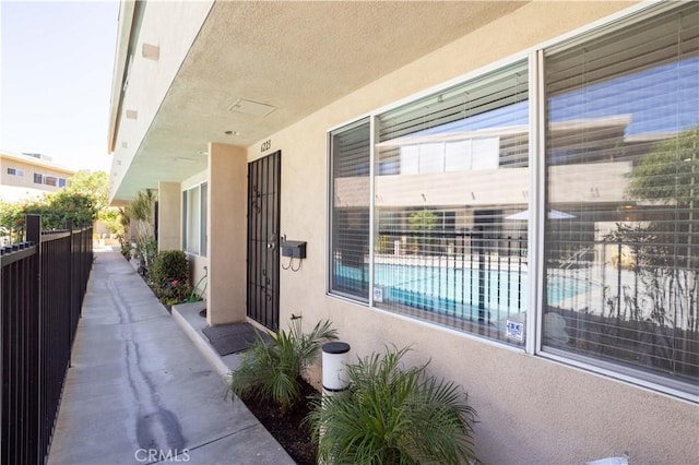 view of exterior entry with stucco siding and fence