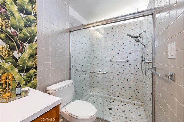 bathroom with toilet, tile walls, vanity, and a shower with shower door