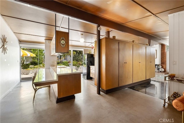 kitchen with black refrigerator, decorative light fixtures, a breakfast bar area, concrete floors, and beam ceiling