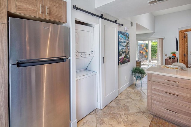 laundry room featuring light tile patterned floors, a barn door, and stacked washer and dryer