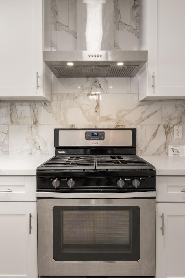 kitchen featuring white cabinetry, wall chimney range hood, gas range, and backsplash