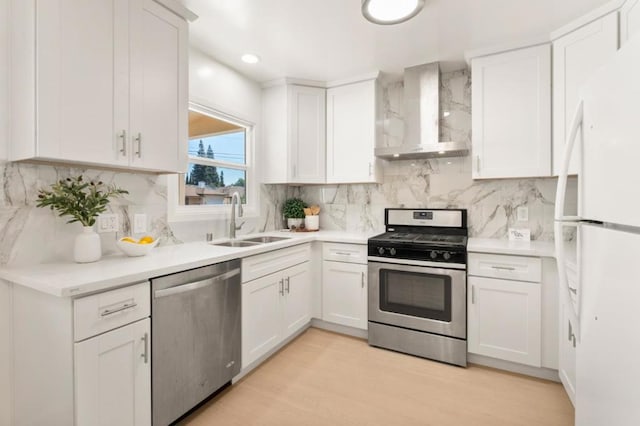 kitchen featuring wall chimney range hood, stainless steel appliances, sink, and white cabinets