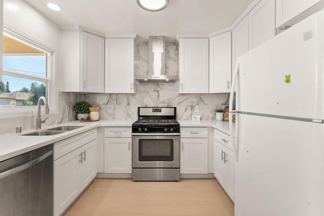 kitchen with wall chimney exhaust hood, appliances with stainless steel finishes, sink, and white cabinets