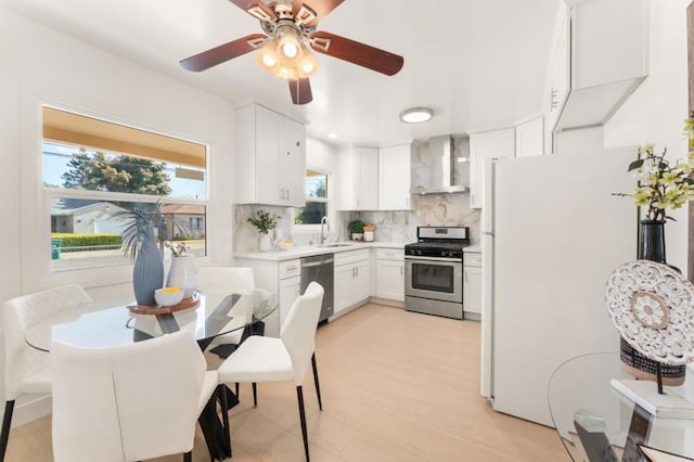 kitchen with wall chimney exhaust hood, sink, white cabinetry, appliances with stainless steel finishes, and backsplash