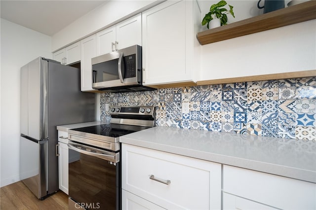 kitchen with decorative backsplash, stainless steel appliances, white cabinets, and light wood-type flooring