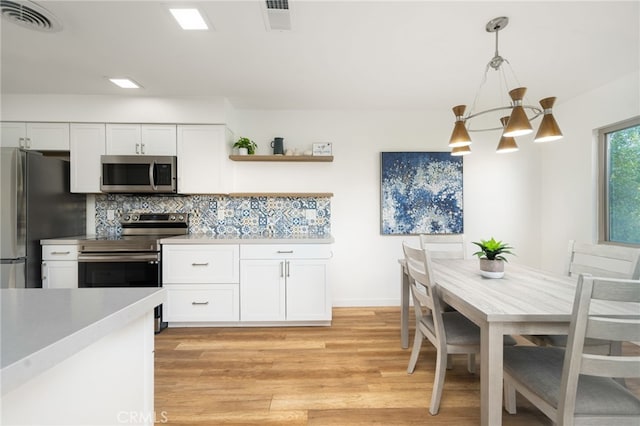 kitchen with hanging light fixtures, white cabinetry, stainless steel appliances, a notable chandelier, and light hardwood / wood-style floors