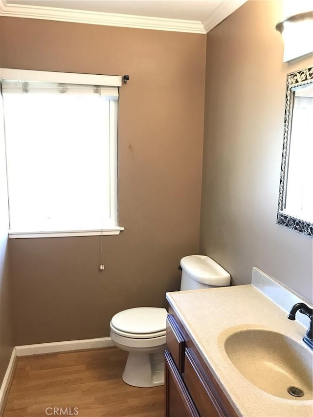 bathroom featuring vanity, wood finished floors, baseboards, ornamental molding, and toilet