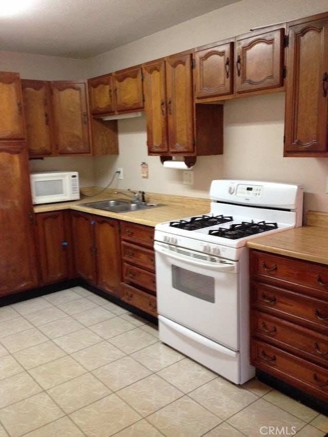 kitchen with brown cabinetry, white appliances, light countertops, and a sink