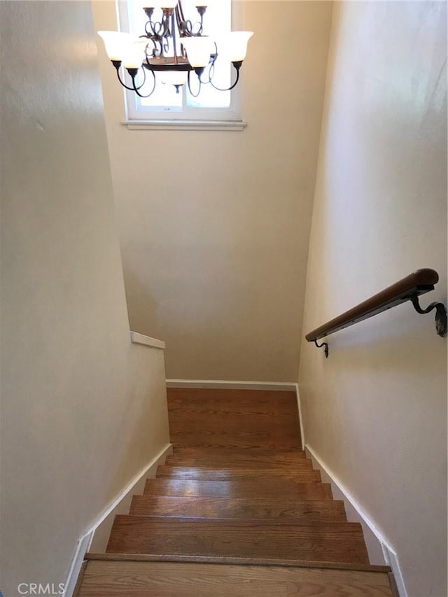 stairs with wood finished floors, baseboards, and a chandelier